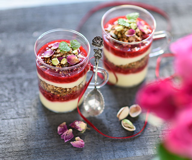 Schichtdessert im Glas mit Pistazien-Tahini-Rosenblütenblätter-Granola, Vanille-Joghurt-Creme und Himbeeren